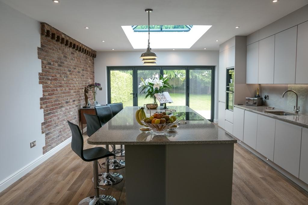 Grey handleless kitchen with granite island, exposed brick feature wall and lantern roof light in a Hampshire home extension by Kitchen Living