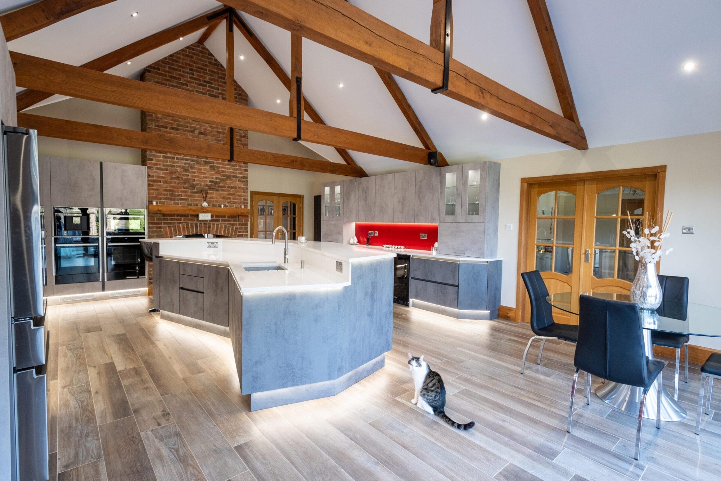 Kitchen Living modern handleless kitchen with exposed beams, white island, red cooker hood and open-plan living space