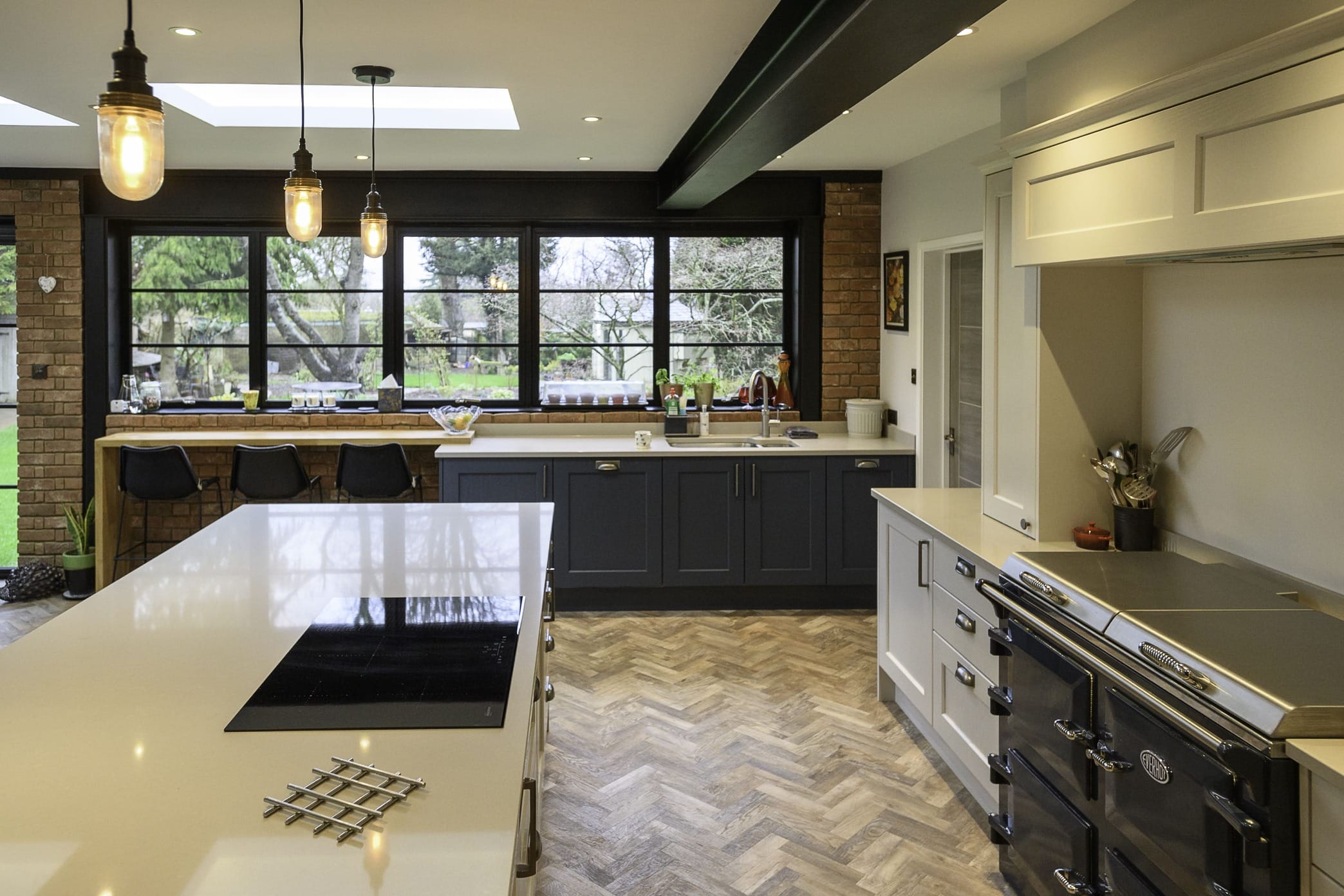 Dark navy and white shaker kitchen with AGA range cooker, quartz island, herringbone parquet floor and exposed brick feature wall by Kitchen Living