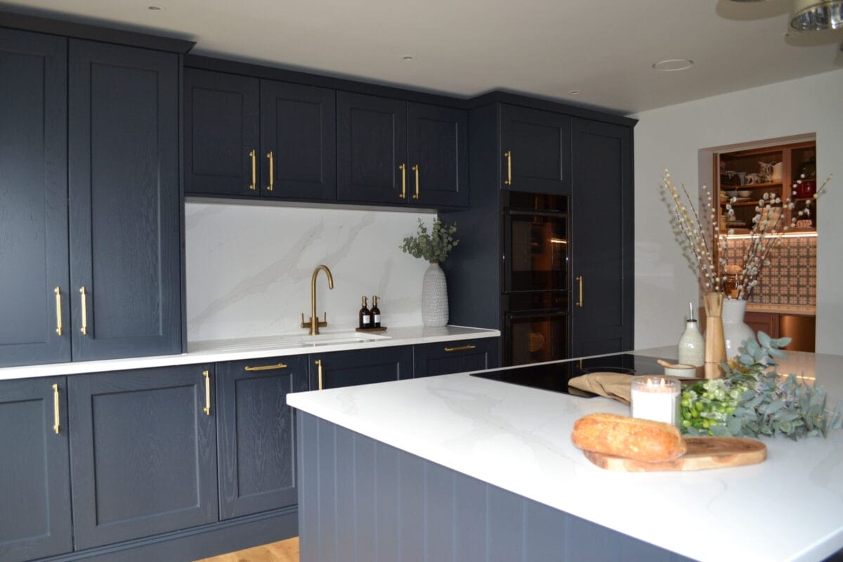 Bespoke dark blue shaker kitchen with island, white quartz worktops and brass handles by Kitchen Living