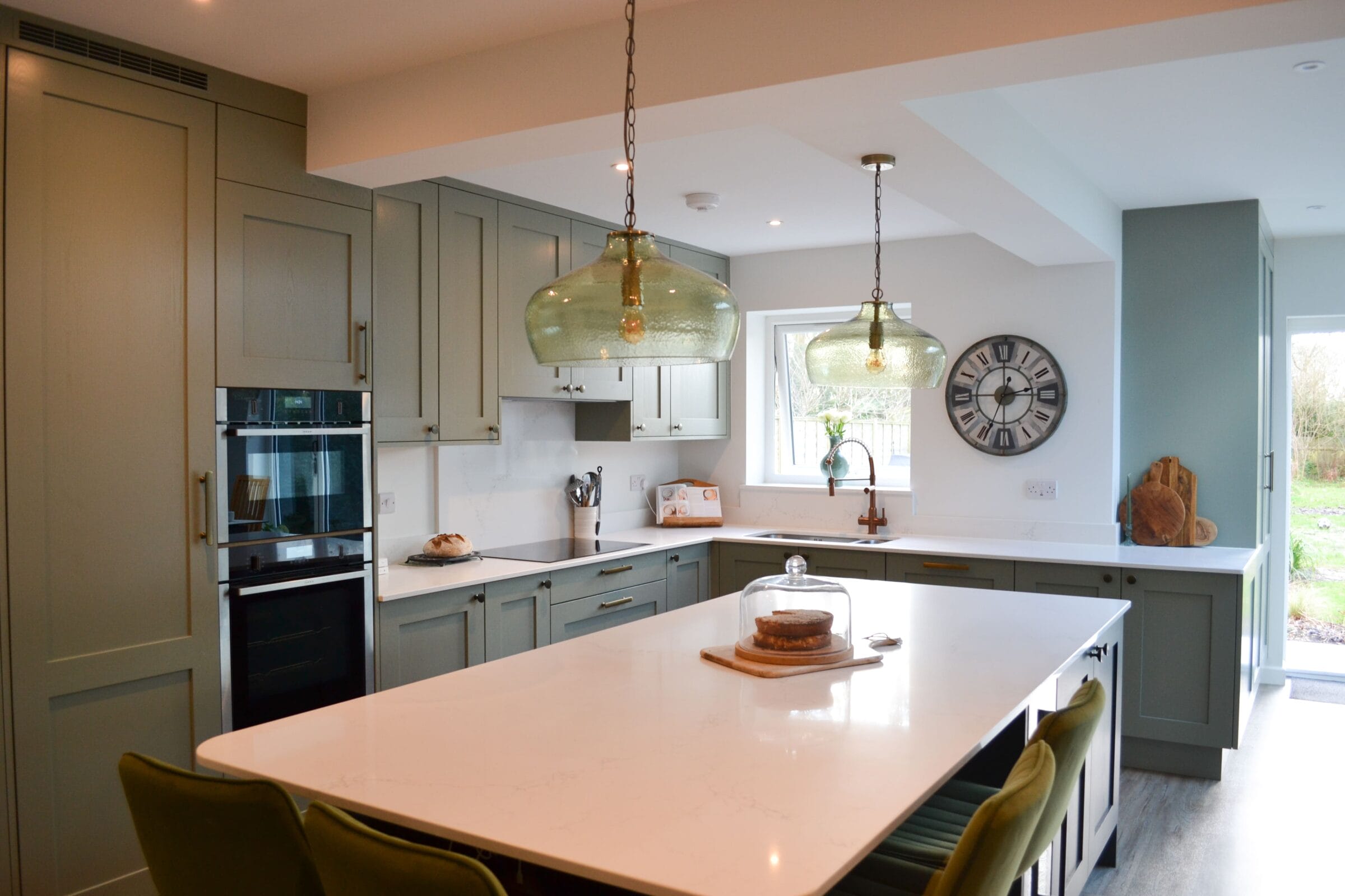 age green shaker kitchen with white quartz island, green glass pendant lights and integrated appliances by Kitchen Living Winchester