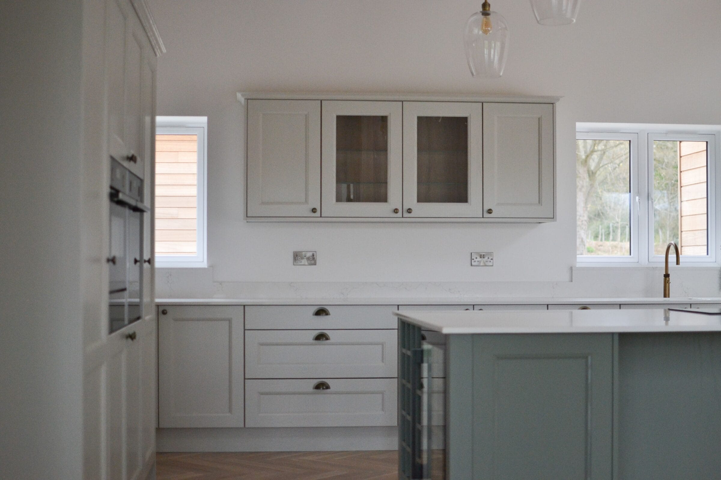 Off-white in-frame shaker kitchen cabinets with black cup handles, quartz worktop and sage green island detail by Kitchen Living Winchester